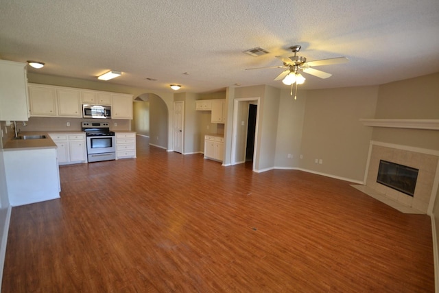 unfurnished living room featuring sink, ceiling fan, a fireplace, a textured ceiling, and dark hardwood / wood-style flooring