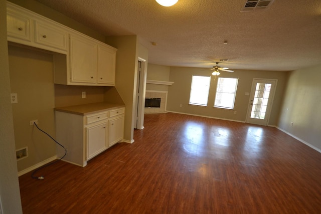 unfurnished living room featuring a tile fireplace, dark hardwood / wood-style floors, a textured ceiling, and ceiling fan