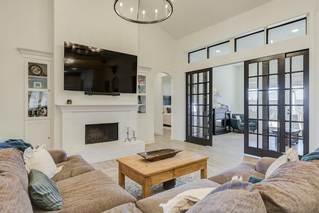 4309 136th St, Lubbock, TX 79423 - living room featuring arched walkways, a chandelier, a towering ceiling, wood finished floors, and a brick fireplace