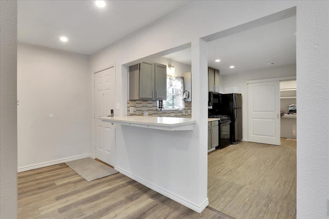 kitchen with gray cabinets, light hardwood / wood-style flooring, decorative backsplash, and black appliances