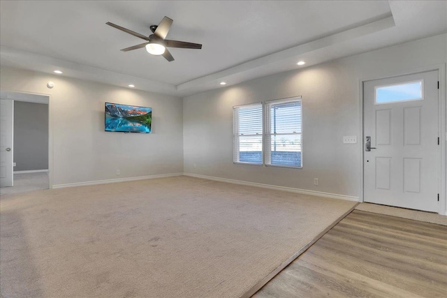 carpeted foyer with a raised ceiling and ceiling fan