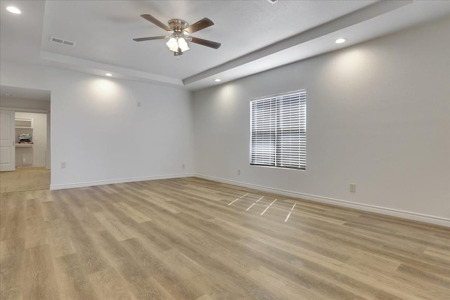 spare room featuring ceiling fan, a tray ceiling, and light hardwood / wood-style flooring