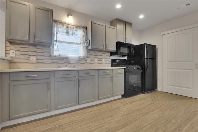 kitchen featuring gray cabinetry, light wood-type flooring, tasteful backsplash, and black appliances