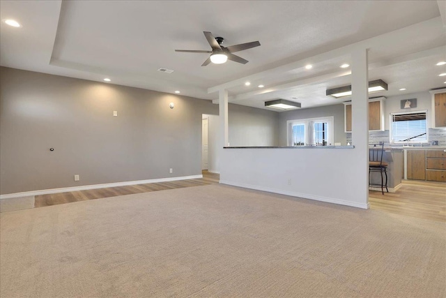 unfurnished living room featuring ceiling fan, a raised ceiling, and light colored carpet