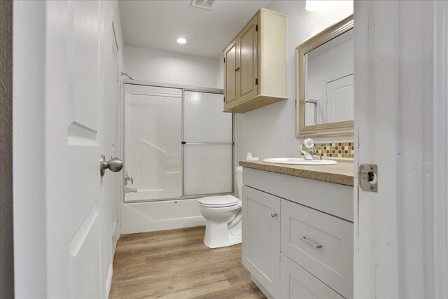 full bathroom with hardwood / wood-style floors, backsplash, shower / bath combination with glass door, vanity, and toilet