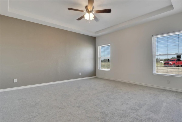 empty room with a raised ceiling, light carpet, and ceiling fan