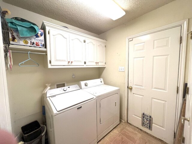 clothes washing area with cabinets, washing machine and clothes dryer, and a textured ceiling