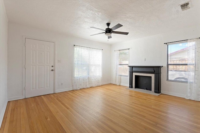 unfurnished living room with ceiling fan, a wealth of natural light, a textured ceiling, and light hardwood / wood-style floors