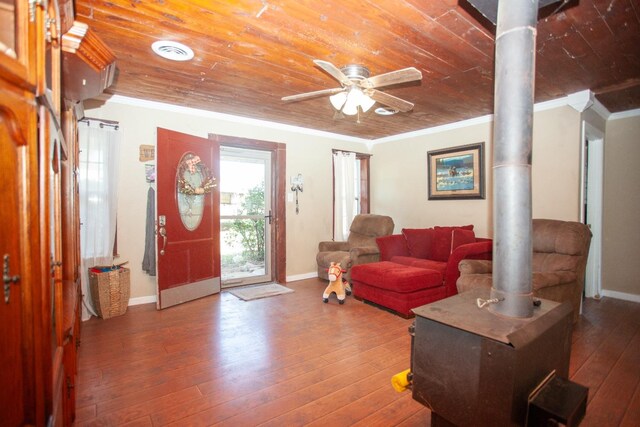 living room with hardwood / wood-style floors, a wood stove, ornamental molding, ceiling fan, and wooden ceiling