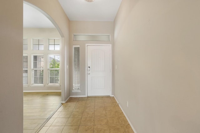 foyer entrance featuring arched walkways, baseboards, and light tile patterned floors