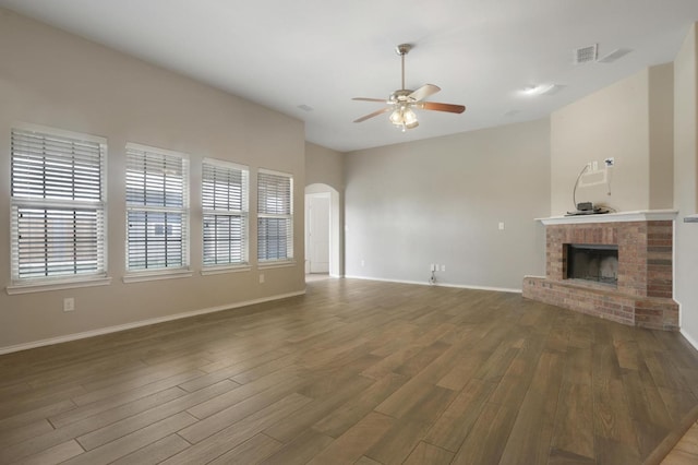 unfurnished living room with arched walkways, ceiling fan, a fireplace, wood finished floors, and visible vents