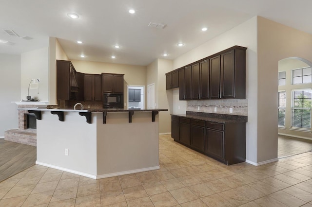 kitchen featuring black microwave, dark brown cabinetry, a peninsula, and a breakfast bar area