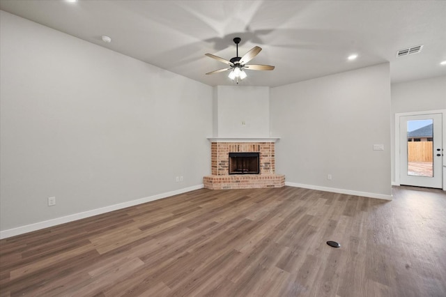 unfurnished living room featuring ceiling fan, wood-type flooring, and a brick fireplace