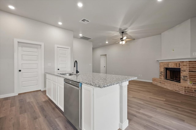 kitchen featuring dishwasher, an island with sink, white cabinets, light stone countertops, and a brick fireplace