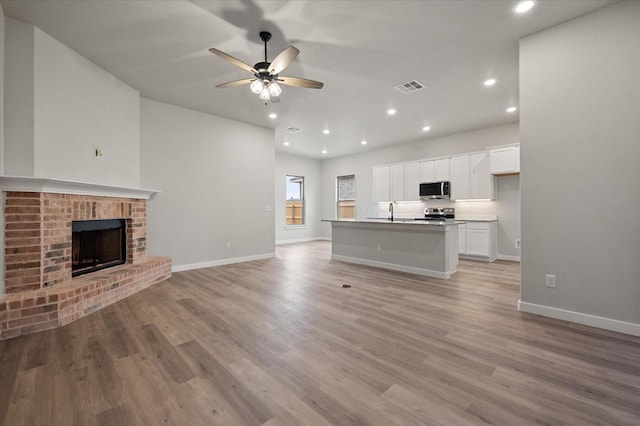 unfurnished living room with sink, light hardwood / wood-style flooring, a fireplace, and ceiling fan