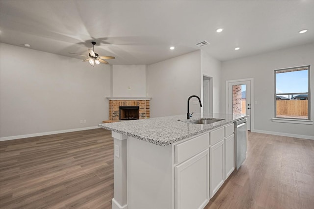 kitchen with white cabinetry, sink, light stone countertops, a center island with sink, and a brick fireplace