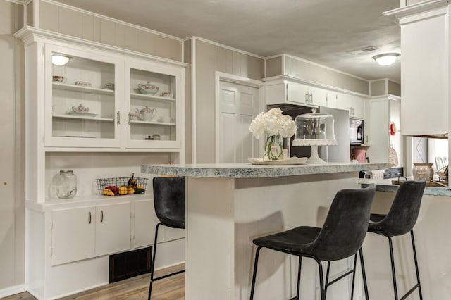 kitchen with a kitchen bar, kitchen peninsula, light hardwood / wood-style flooring, and white cabinets