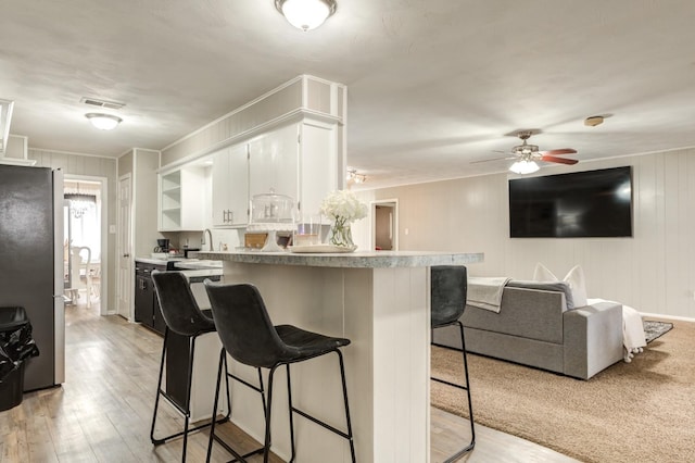 kitchen with white cabinetry, a breakfast bar, stainless steel fridge, and light wood-type flooring