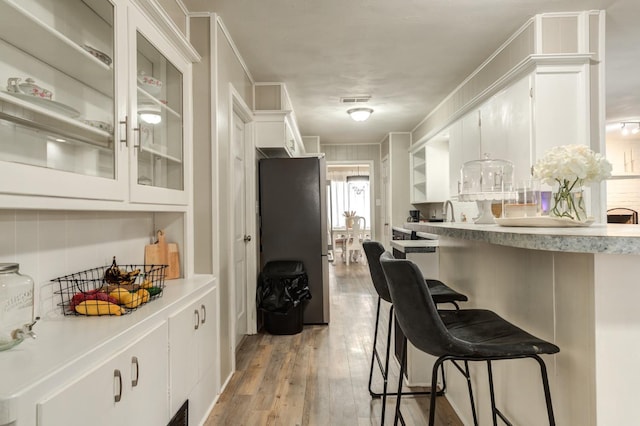 kitchen with crown molding, light hardwood / wood-style flooring, a breakfast bar area, stainless steel refrigerator, and white cabinetry