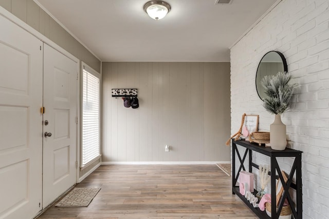 entryway with crown molding, brick wall, light wood-type flooring, and a wealth of natural light