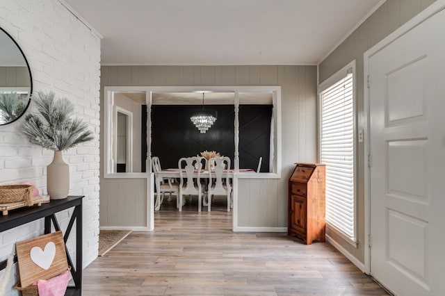 interior space featuring an inviting chandelier, crown molding, wooden walls, and light hardwood / wood-style floors