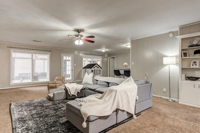 carpeted living room with ceiling fan and wood walls