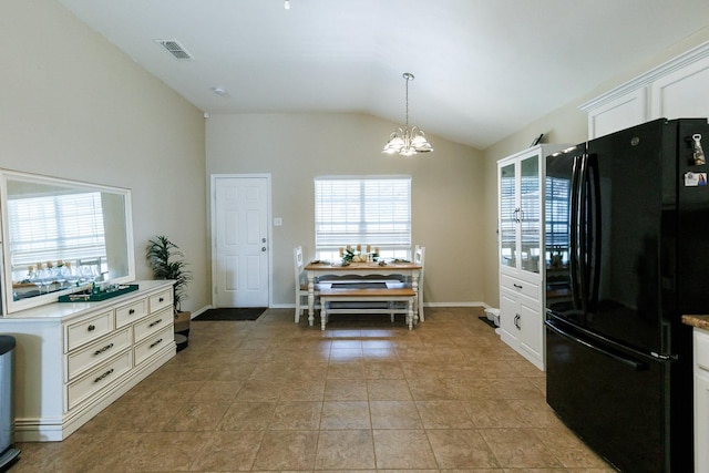 kitchen featuring lofted ceiling, light tile patterned floors, black refrigerator, a notable chandelier, and white cabinets