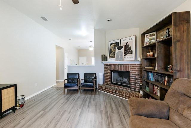 living room with ceiling fan, a fireplace, and light wood-type flooring