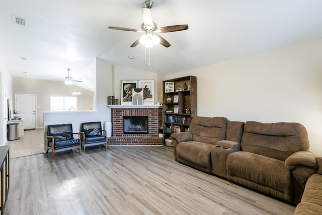 living room featuring ceiling fan, vaulted ceiling, a brick fireplace, and light wood-type flooring