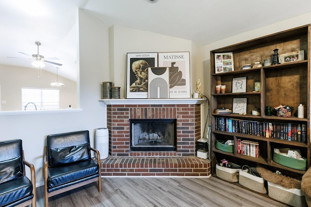 living area with a fireplace, vaulted ceiling, wood-type flooring, and ceiling fan