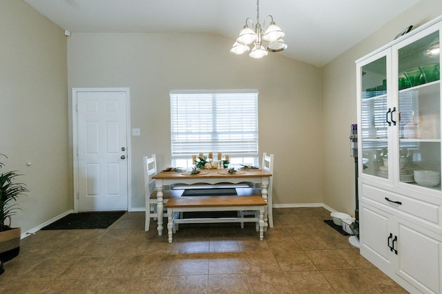 dining area with lofted ceiling, dark tile patterned flooring, and an inviting chandelier