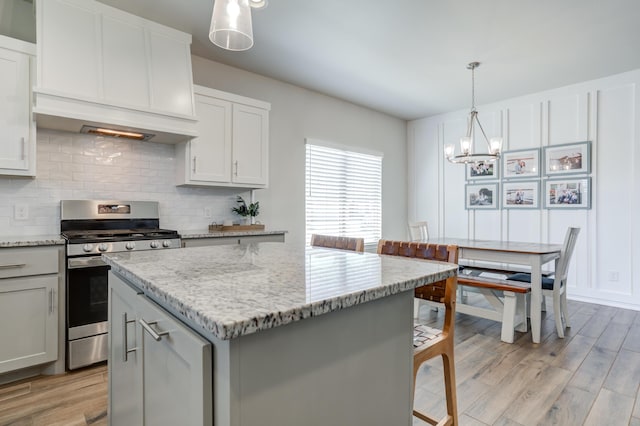 kitchen featuring light stone countertops, an inviting chandelier, decorative backsplash, light wood-style floors, and stainless steel range with gas cooktop
