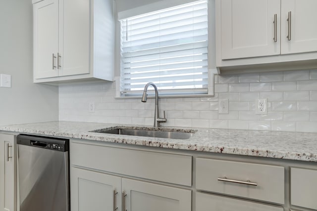 kitchen featuring light stone countertops, backsplash, dishwasher, and a sink