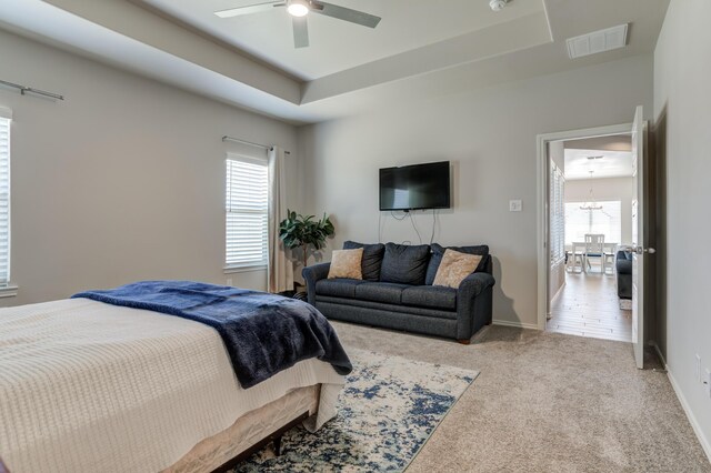carpeted bedroom featuring baseboards, visible vents, ceiling fan with notable chandelier, and a tray ceiling