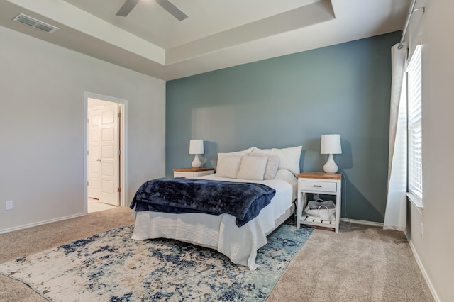 carpeted bedroom featuring ensuite bathroom, baseboards, visible vents, a raised ceiling, and a ceiling fan