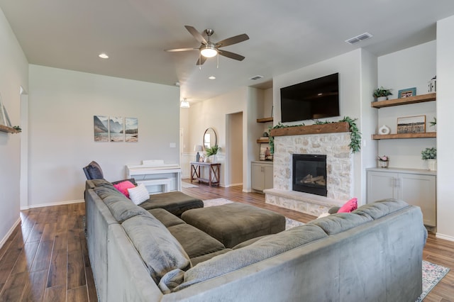 living room featuring a ceiling fan, a stone fireplace, visible vents, baseboards, and wood finished floors