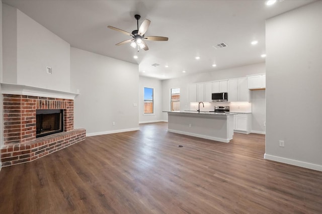 unfurnished living room with ceiling fan, dark hardwood / wood-style flooring, sink, and a fireplace