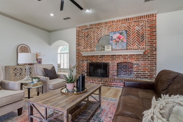 living room featuring crown molding, hardwood / wood-style floors, a brick fireplace, and a textured ceiling