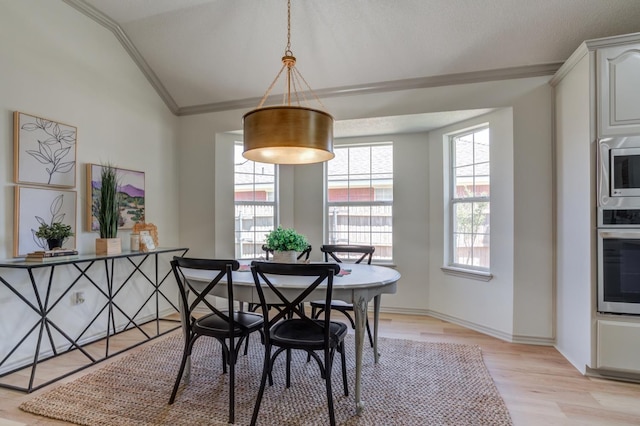 dining space with crown molding, vaulted ceiling, and light hardwood / wood-style flooring