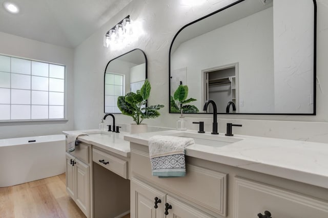 bathroom with vaulted ceiling, vanity, a tub, and wood-type flooring