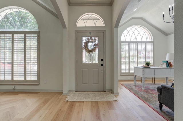 entrance foyer featuring ornamental molding, vaulted ceiling, an inviting chandelier, and light hardwood / wood-style floors