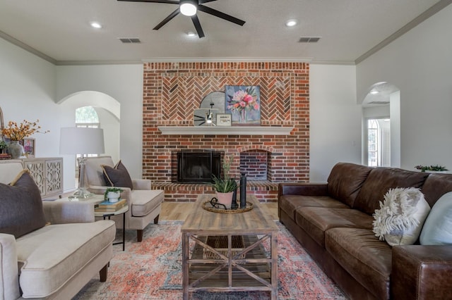 living room featuring ceiling fan, ornamental molding, hardwood / wood-style floors, and a brick fireplace