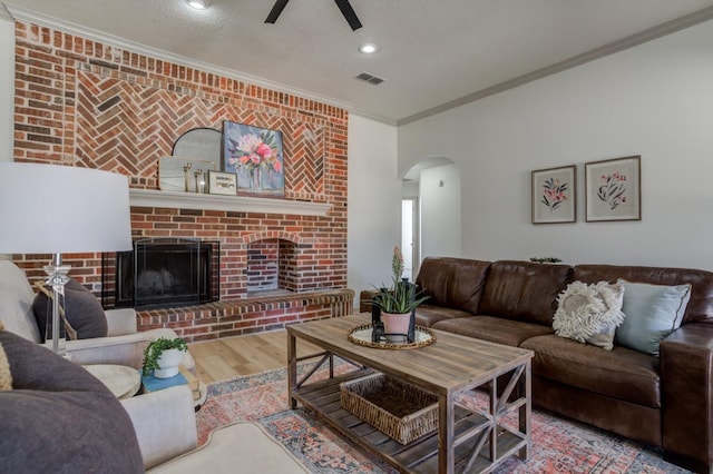 living room with crown molding, ceiling fan, hardwood / wood-style floors, a fireplace, and a textured ceiling