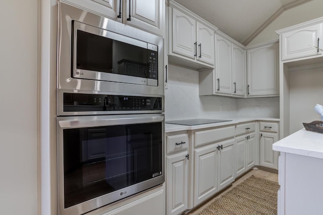 kitchen featuring vaulted ceiling, white cabinetry, appliances with stainless steel finishes, and decorative backsplash