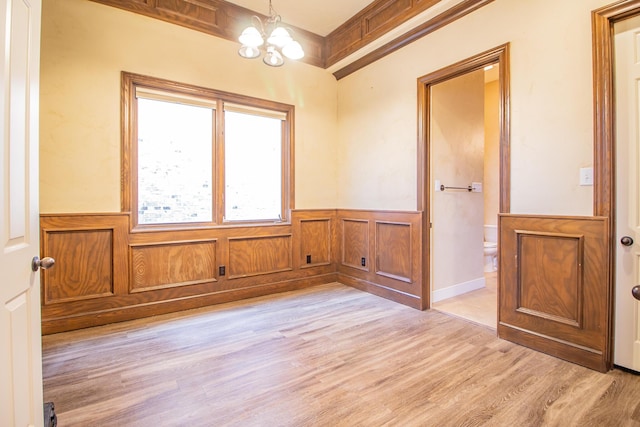 empty room featuring light wood finished floors, a wainscoted wall, and a notable chandelier