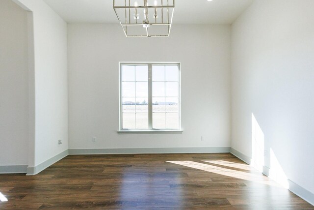 empty room with baseboards, a notable chandelier, and wood finished floors