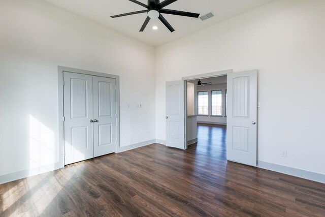 unfurnished bedroom with a closet, dark hardwood / wood-style floors, ceiling fan, and a towering ceiling