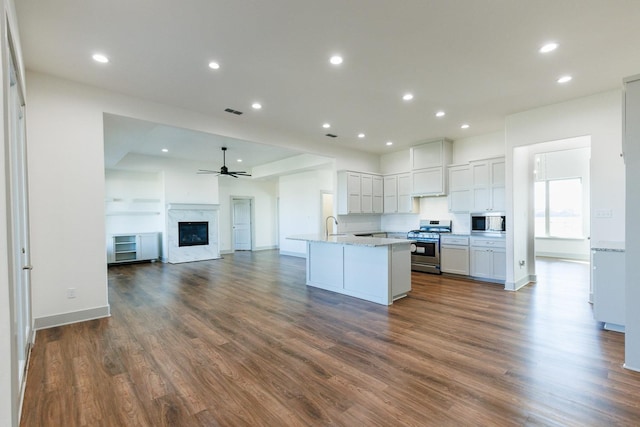 kitchen featuring dark wood-type flooring, ceiling fan, appliances with stainless steel finishes, white cabinetry, and a kitchen island with sink