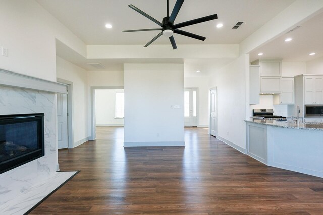 unfurnished living room featuring ceiling fan, a premium fireplace, dark hardwood / wood-style floors, and sink