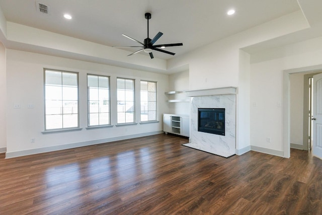 unfurnished living room with dark wood-type flooring, baseboards, a tray ceiling, a fireplace, and a ceiling fan